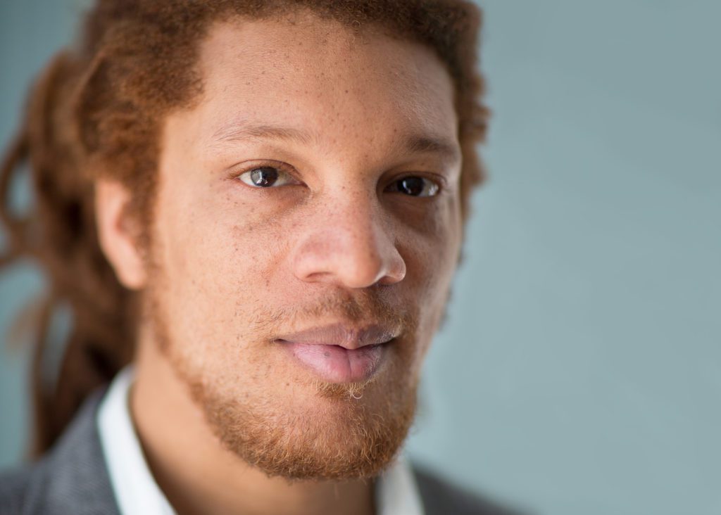 A close view of D. Fox Harrell looking directly into the camera against a green-blue background.