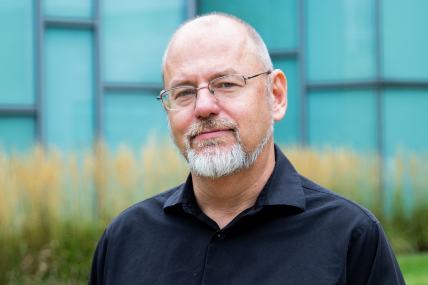 Headshot of Stefan Helmriech standing in front of a blue glass building and a fringe of tall grass.